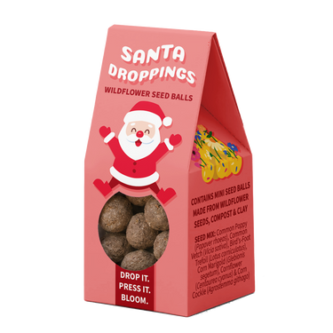 A pink triangular stand-up box labeled 'Santa Droppings Wildflower Seed Balls' with a large Santa illustration on the front, a clear window showing round seed balls inside, and product text on the side. The box is photographed on a plain white background.
