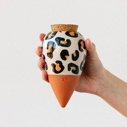 Hand holding a terracotta pot with a leopard print design on a light gray background